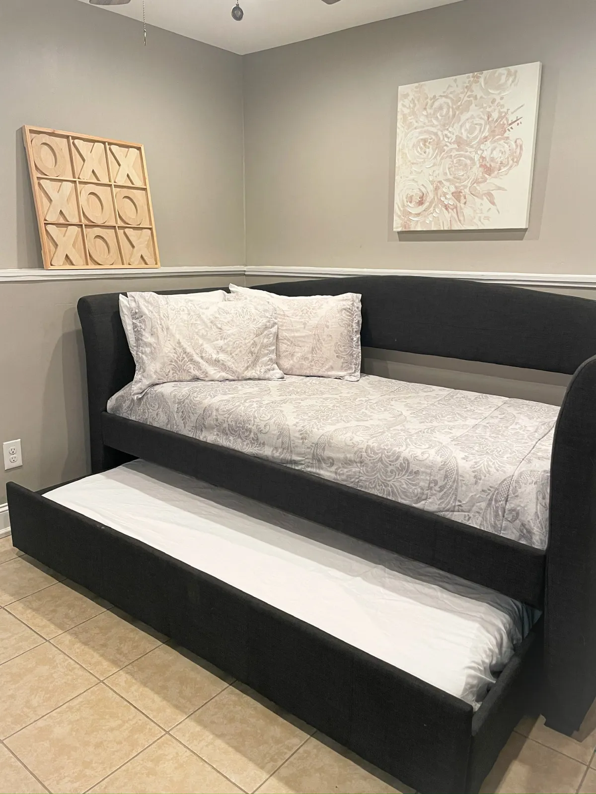 The image features a daybed adorned with decorative pillows, complemented by vibrant wall art including floral motifs and a tic-tac-toe board. The space feels inviting and relaxed, ideal for reading, relaxing, or accommodating group sleepovers.
