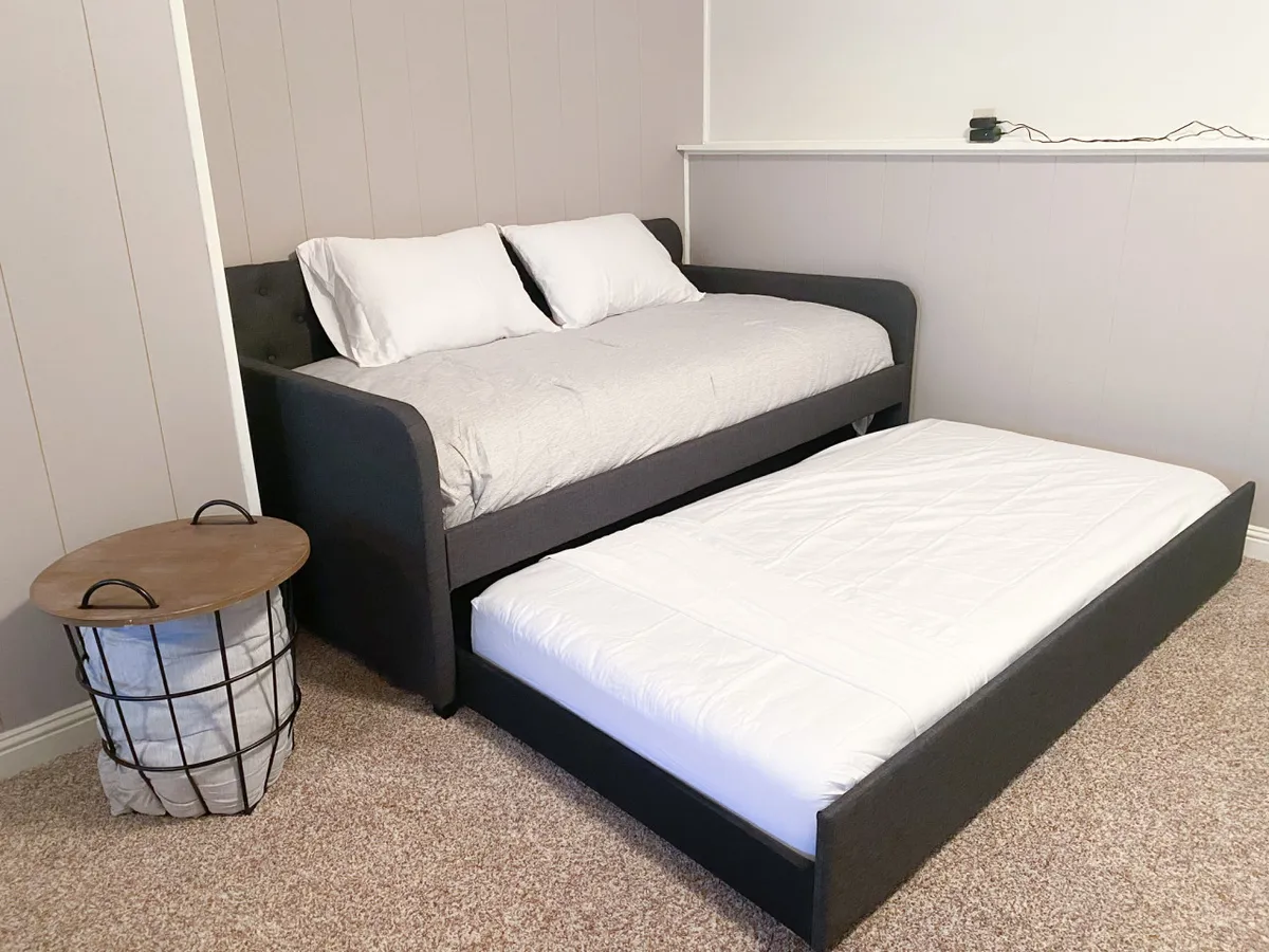 A flexible sleeping nook with a stylish daybed, an underbed trundle for additional guests, and a compact side table. The setup is cozy and practical, illustrating adaptable sleeping arrangements for different group needs.
